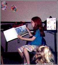 Picture of Jordan reading her book to the kids at Story Time at the library